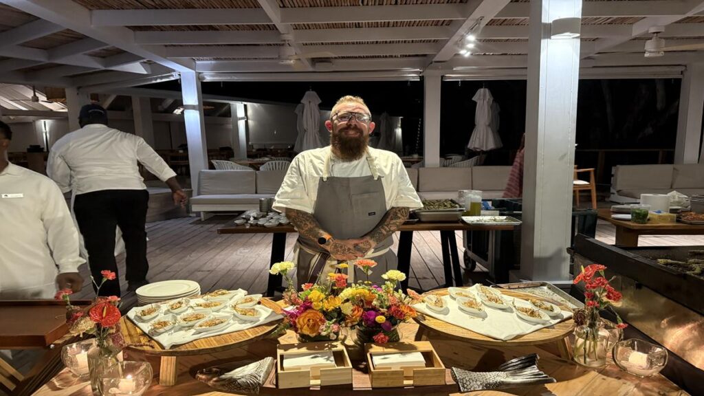 Guest chef standing behind a decorated food station at Minitas Beach Club